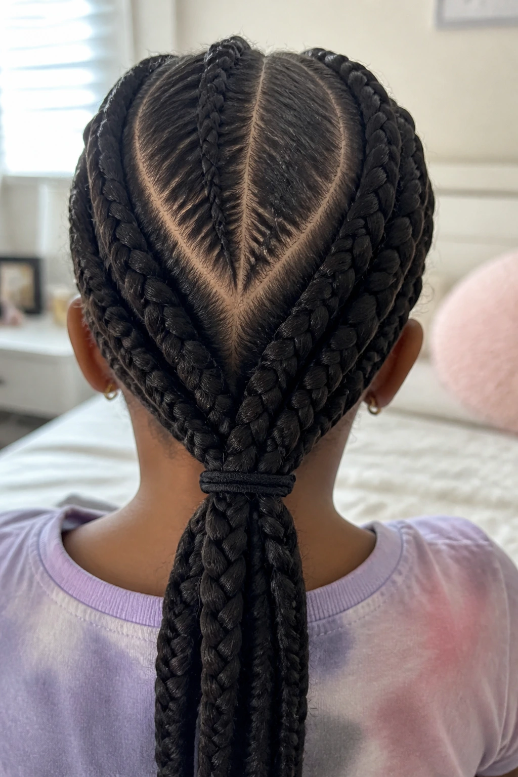 Back view of a girl with V-shaped back-part braids in bright bedroom.