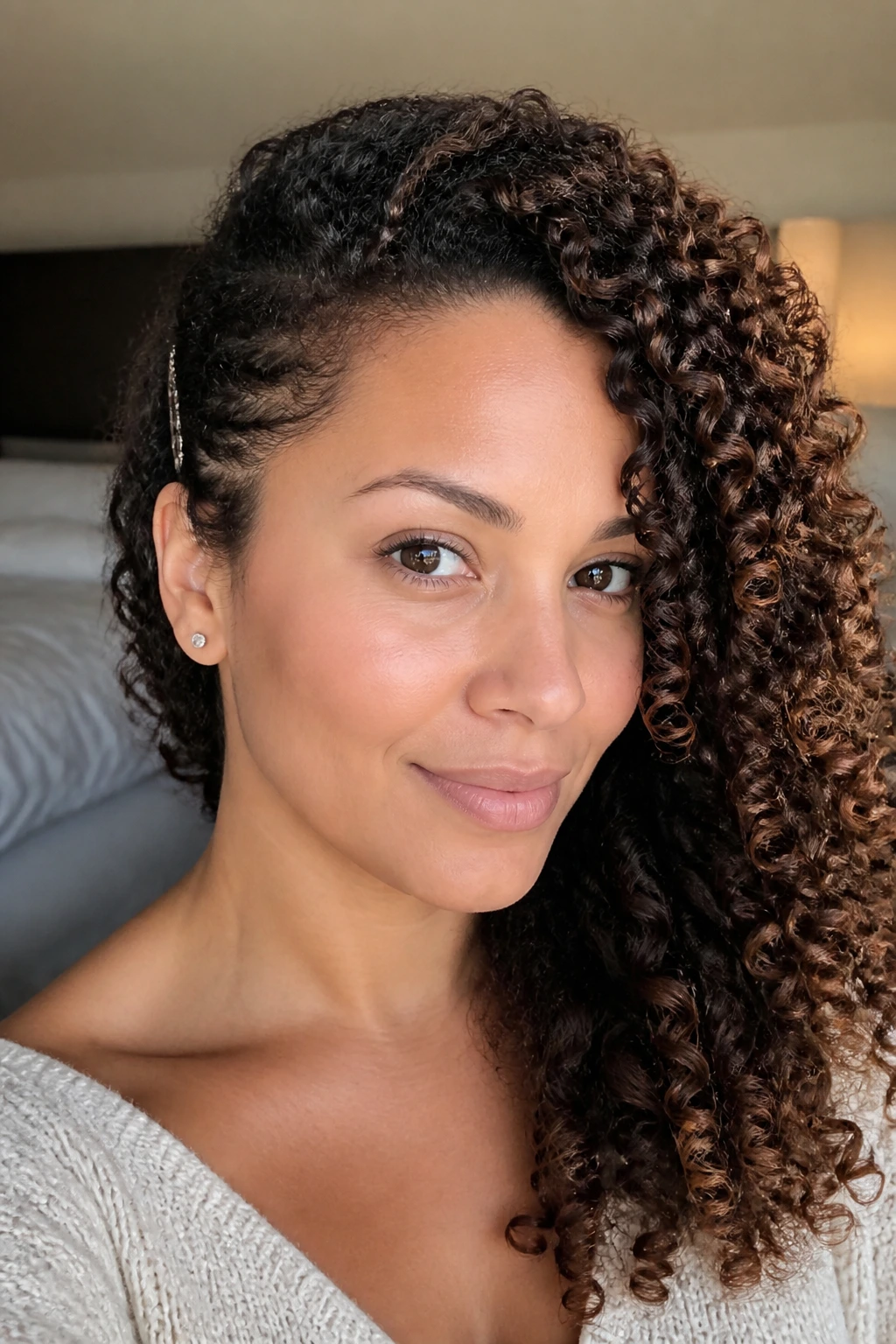 Close-up of a real woman with defined curls and an ear tuck highlighting lowlights.